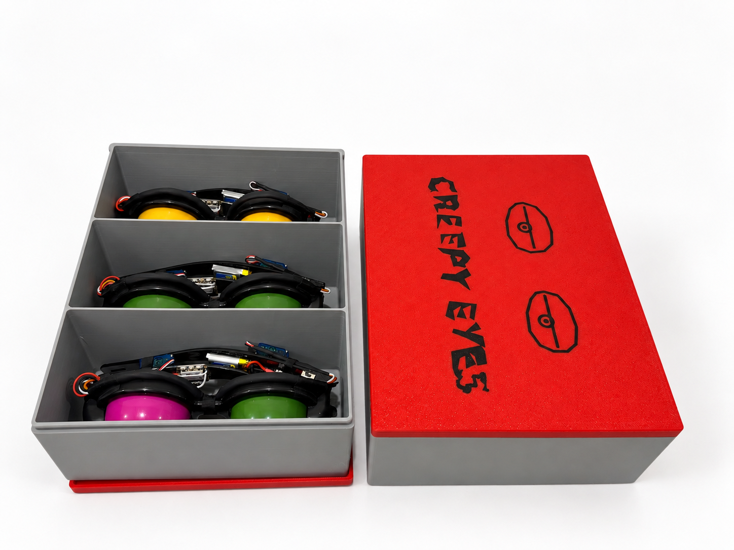 Open gray and red 3D-printed Creepy Eyes case holding five working Creeps in divided compartments beside its red lid